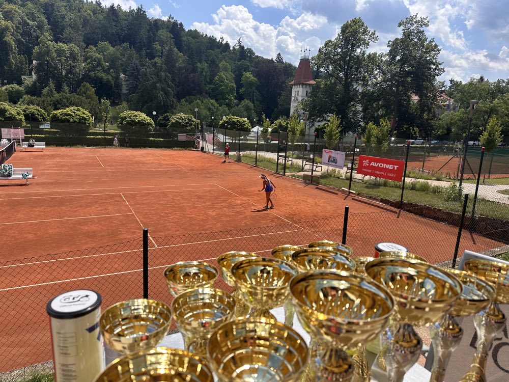 Poháry připravené pro účastníky AVONET CUP 2026 s pohledem na kurty